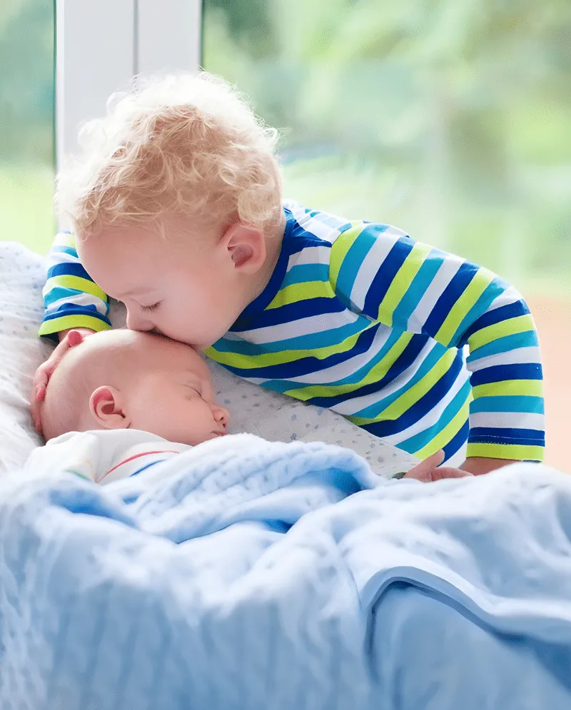 A toddler gently kissing a newborn